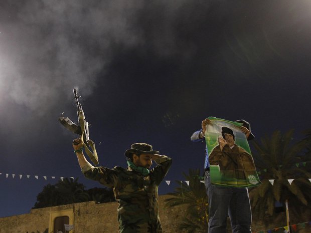 Soldado leal a Kadhafi dá tiros para o ar neste domingo (20) em Trípoli, capital da Líbia, enquanto colega mostra cartaz com a imagem do ditador