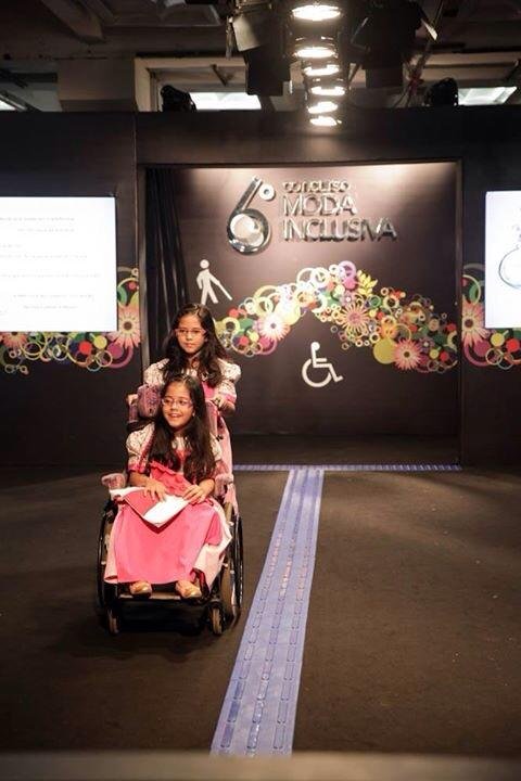 Na passarela, a pequena modelo apresenta a roupa auxiliada pela irmã gêmea na condução da cadeira de rodas - Foto: Coordenadora de Imprensa  Cesumar