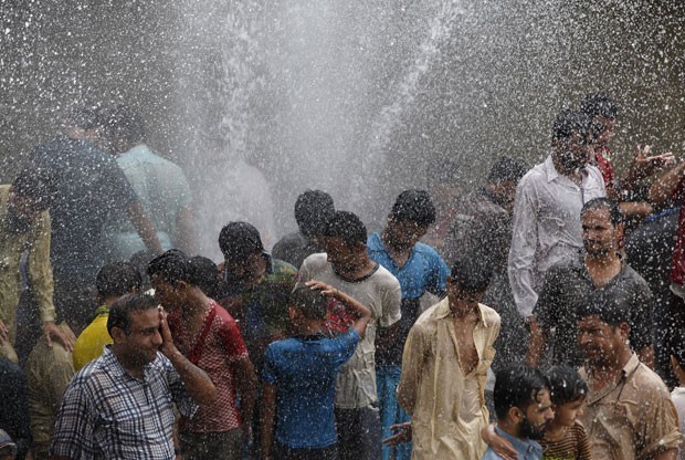 Pessoas se aliviam do forte calor com spray de água em Karachi, no Paquistão, nesta quinta-feira (25) (Foto: Akhtar Soomro/Reuters)